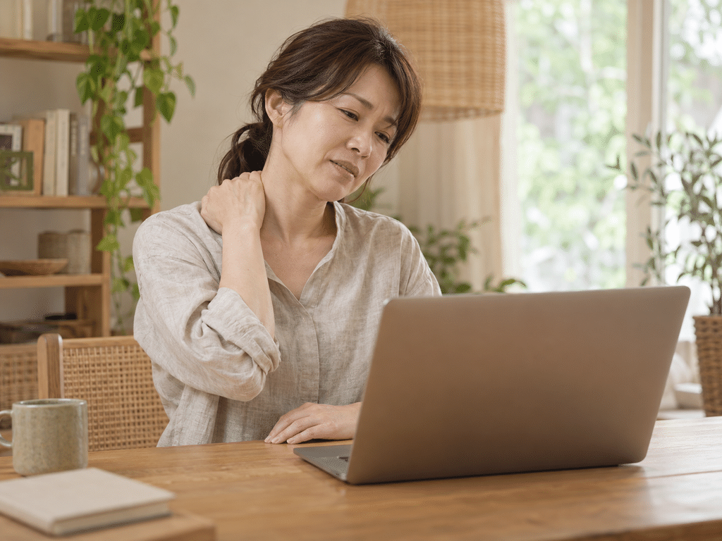 デスクワーク中に首から肩をもんでいる女性